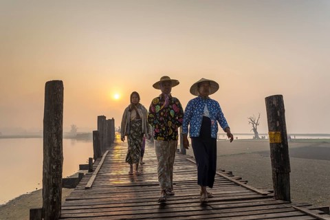 Women wearing traditional hats on a teak bridge