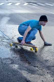 Teenager riding a longboard downhill on a wet street