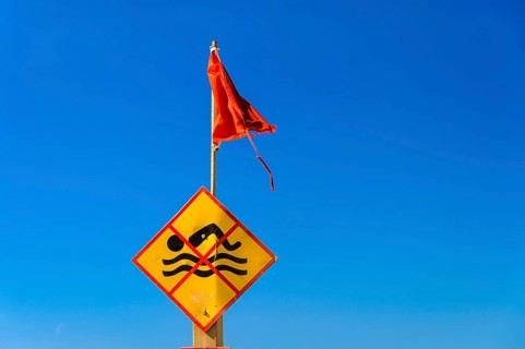 Bathing prohibition sign with red flag in front of a blue sky