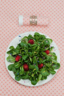Lamb's lettuce with strawberries and flower petals served on a plate