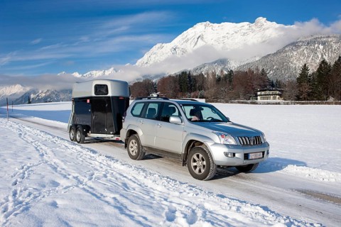 Four wheel drive vehicle towing a horse trailer on a snow-covered road in the mountains
