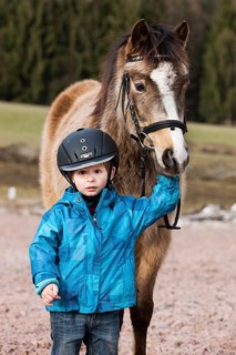 Young child wearing a riding helmet standing beside a pony