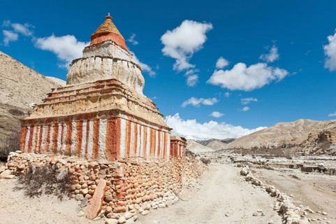 Colourfully decorated Buddhist stupa on a track in a vast landscape