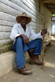 Old man with stick sitting in front of the house