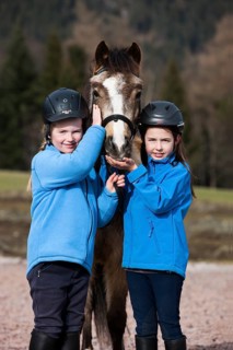 Two girls wearing riding helmets standing beside a pony