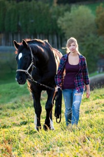 A young woman and a black Hanoverian horse walking on a mountain meadow