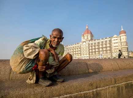 A beggar is sitting in front of the luxurios Taj Mahal Palace Hotel in the suburb Colaba