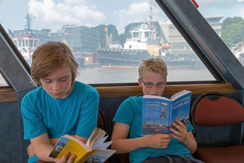 Young people on a language trip read an English travel guide on the Elbe ferry