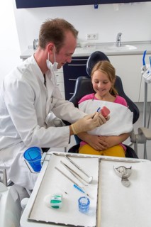 Dentist showing a girl the proper use of a toothbrush