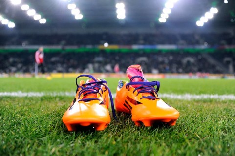 Orange-coloured Adidas football boots on the edge of the pitch
