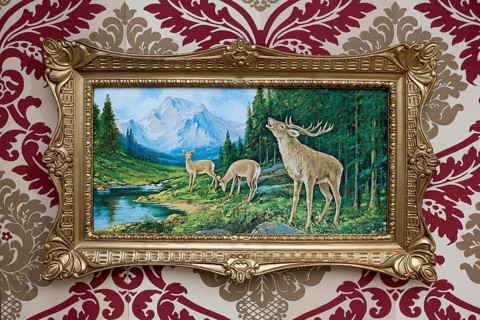 Trashy deer picture in a plastic gold frame on patterned wallpaper