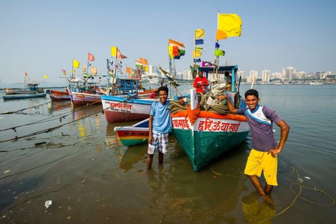 Two fishermen and some fishing boats in front of the skyline of the suburb Churchgate seen across the Back Bay