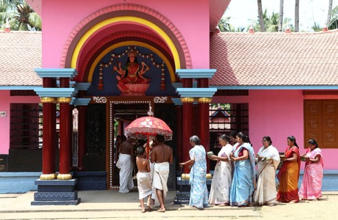 A group of women with offerings and a priest circling a Hindu temple