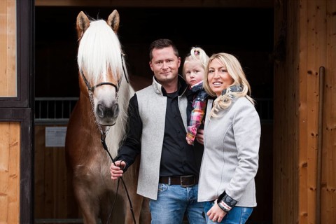 Young family standing with a Tyrolean Haflinger in front of a stall