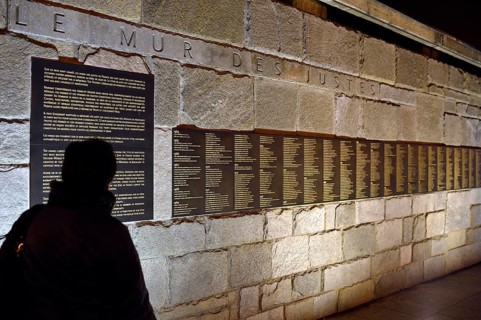 Person standing in front of the Le Mur de Justes plaque at the Memorial de la Shoah