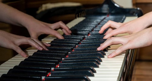Two hands playing a piano and being reflected in the instrument