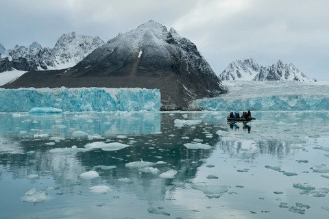 Tourists in a rubber dinghy in front of the rim of the Monacobreen Glacier