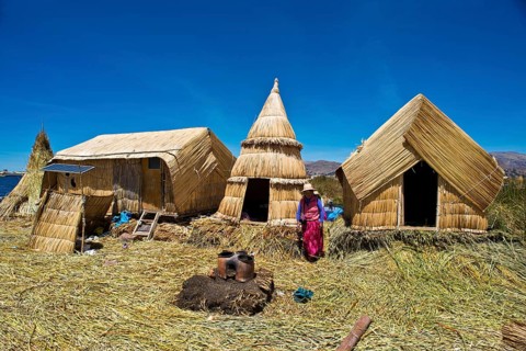 Woman of the Uro Indians in front of typical reed huts