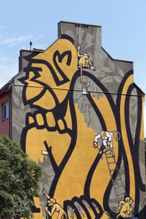 Small monkeys painting a huge monkey on a house wall