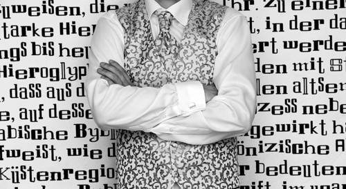 Groom wearing a tie and a waistcoat standing in front of wall with lettering