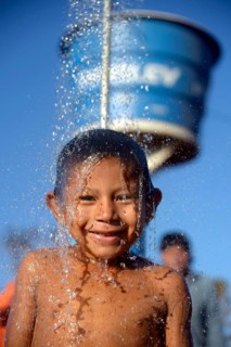 Indian boy of the Xavantes people taking a shower at the water point of a well