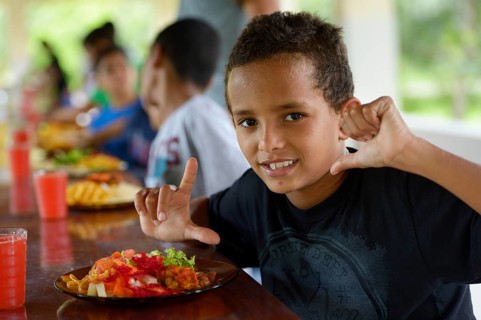 Brazilian boy in front of a full plate of food at the table with other children in a social project for street children
