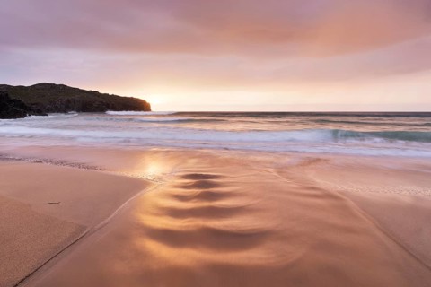 A brook flows over the sandy beach into the sea