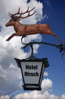 Hanging sign of 'Hotel Hirsch' against a cloudy sky