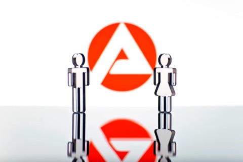 Two figures standing in front of the logo of the German employment agency