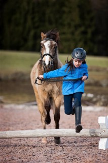 Girl wearing a riding helmet jumping over an obstacle with a pony