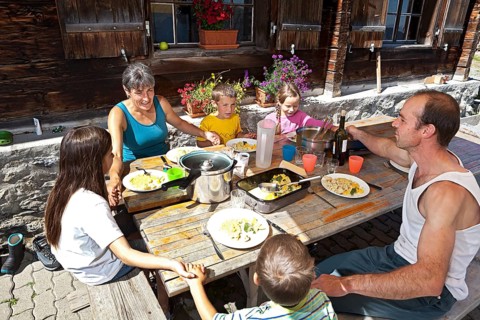 Family holding hands before lunching together in front of a mountain chalet