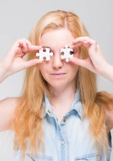 Woman holding two white puzzle pieces in front of her eyes