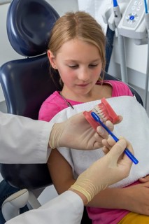 Dentist showing a girl the proper use of a toothbrush