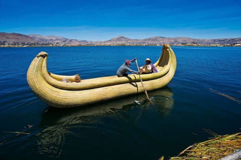 Two local people rowing a traditional boat made of totora reeds on Lake Titicaca