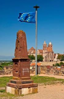Obelisk and the European flag on Eckartsberg hill in front of the historic centre of Breisach with St. Stephansmunster Cathedral