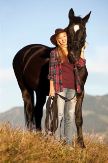 A young woman and a black Hanoverian horse standing on a mountain meadow in autumn