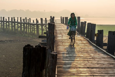 Girl with tanaka on her face riding a bicycle on a teak bridge