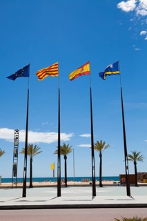 Flags of Spanish regions on flagpoles against blue sky