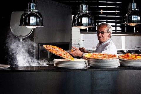 Pizza baker taking the finished pizza out of the oven with a pizza shovel