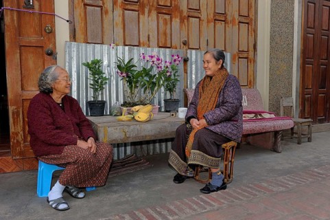 Lao women wearing typical sarongs sitting in front of a house