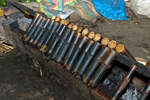 Preparation of the traditional Kralan or Khao Lam rice dish in hollow bamboo tubes over a fire