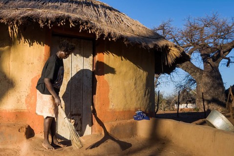 Woman sweeping in front of adobe house