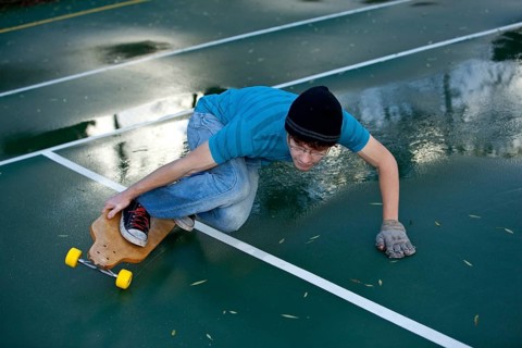 Teenage boy skating with his longboard in a tennis court yard
