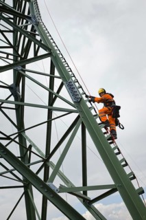 Overhead transmission cable installer climbing a mast to install insulated cable on a newly built high-voltage transmission mast