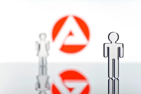 Two figures standing in front of the logo of the German employment agency