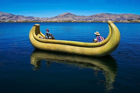 Two local people rowing a traditional boat made of totora reeds on Lake Titicaca
