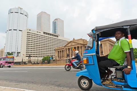 Tuk tuk driver with the building of the Bank of Ceylon at the back