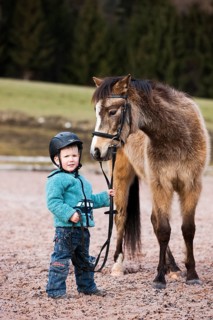 Young child wearing a riding helmet holding a pony