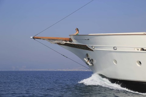 Young woman standing at the bow of a historic yacht and overlooking the sea