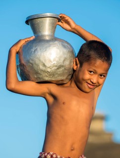 Smiling boy carrying water in a water container made of aluminium